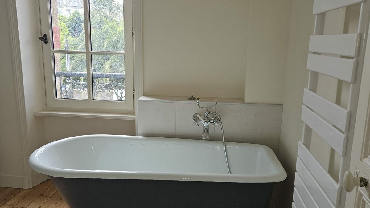 Baignoire ancienne sur pieds rénovée, robinetterie rétro chromée et parquet ancien