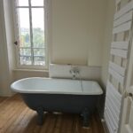 Baignoire ancienne sur pieds rénovée, robinetterie rétro chromée et parquet ancien