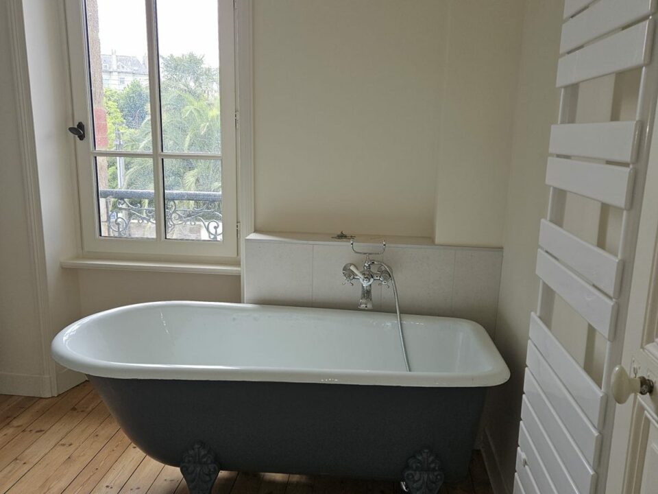 Baignoire ancienne sur pieds rénovée, robinetterie rétro chromée et parquet ancien