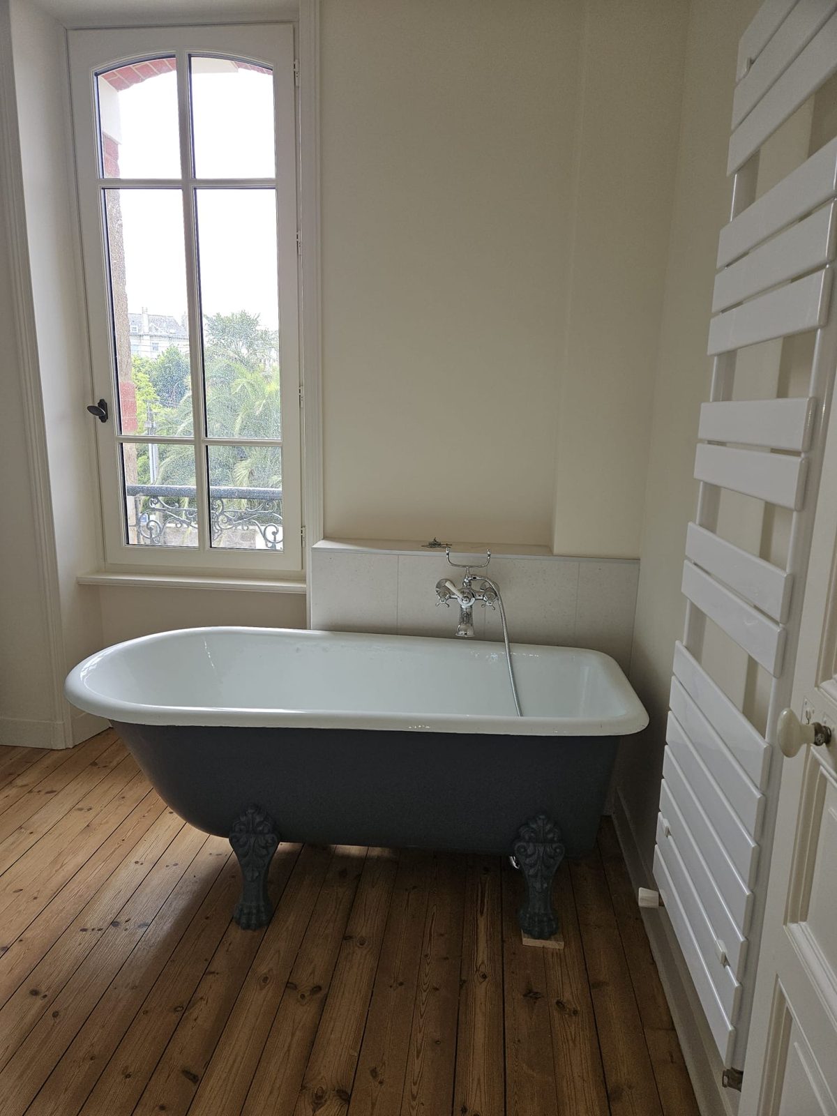 Baignoire ancienne sur pieds dans une salle de bain rénovée à Rennes, avec robinetterie rétro chromée et parquet ancien