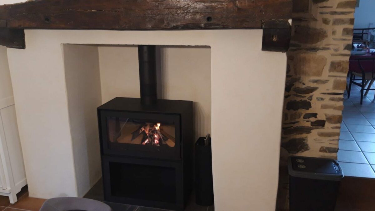 Poêle à bois installé dans une ancienne cheminée rénovée à Rennes, avec poutre en bois et mur en pierre