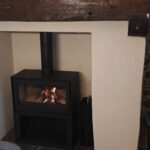 Poêle à bois installé dans une ancienne cheminée rénovée à Rennes, avec poutre en bois et mur en pierre