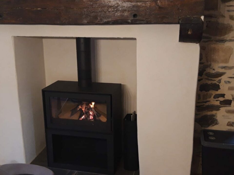 Poêle à bois installé dans une ancienne cheminée rénovée à Rennes, avec poutre en bois et mur en pierre