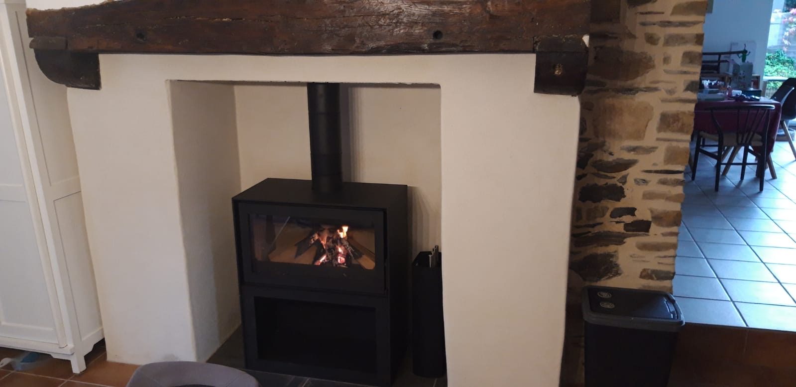 Poêle à bois installé dans une ancienne cheminée rénovée à Rennes, avec poutre en bois et mur en pierre