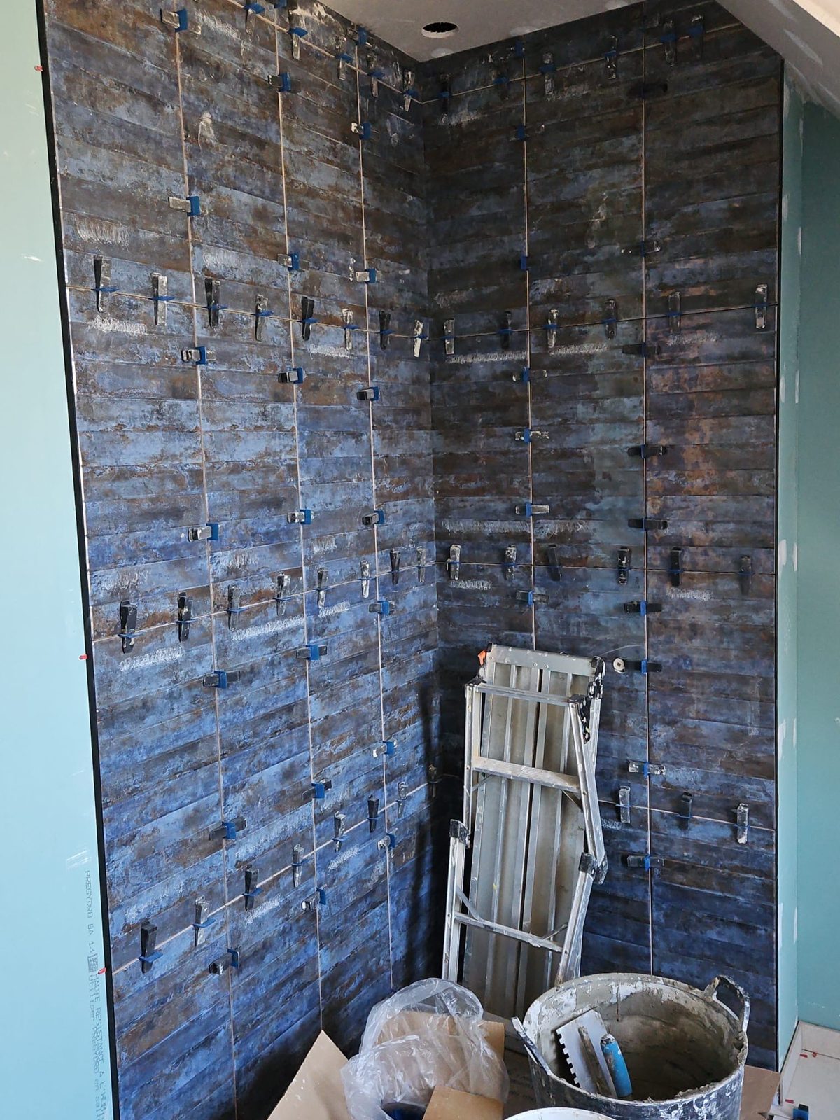 Pose de faïence bleue dans une douche avec système de calage autonivelant pendant le chantier