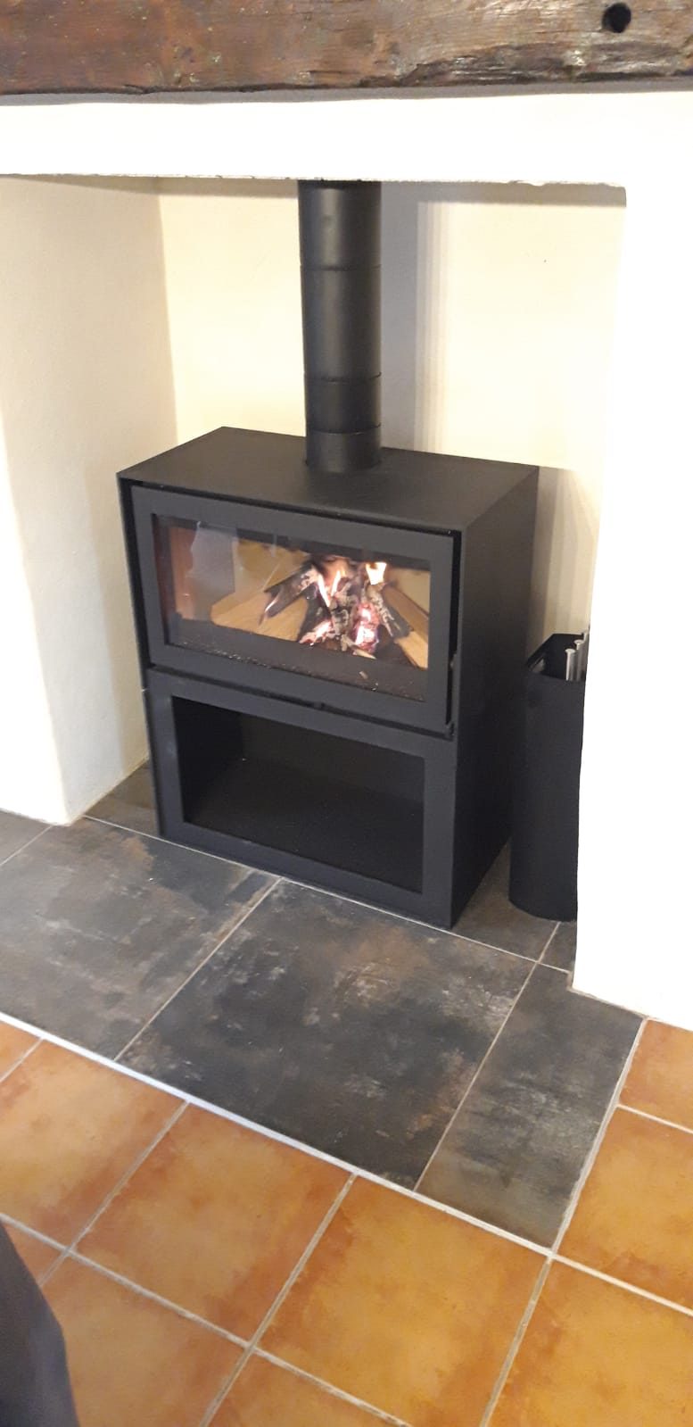 Poêle à bois noir posé dans le foyer d'une ancienne cheminée, sol en carrelage foncé
